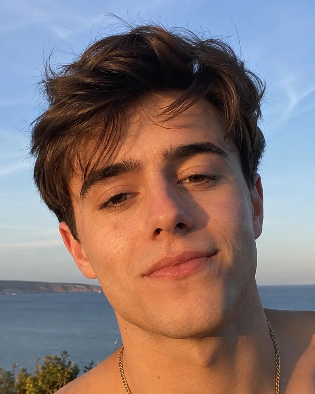 Young man with a gold chain smiling in warm sunlight by the ocean