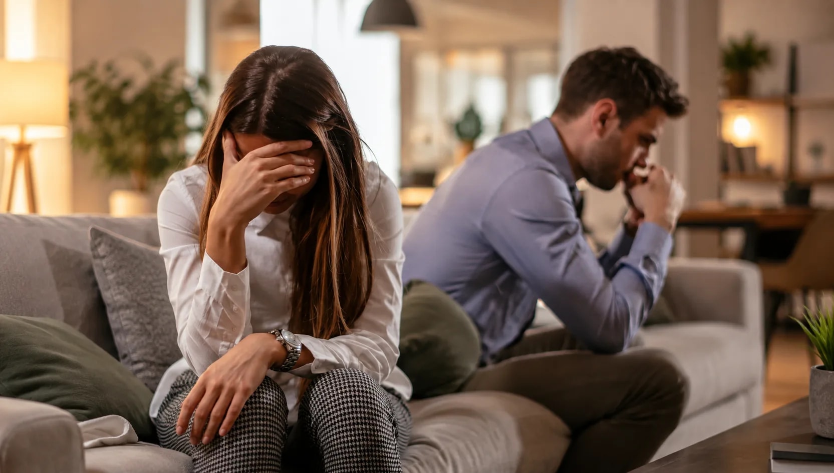 Couple sitting apart on couch with woman distressed and man frustrated, showing emotional distance and avoidance in relationships